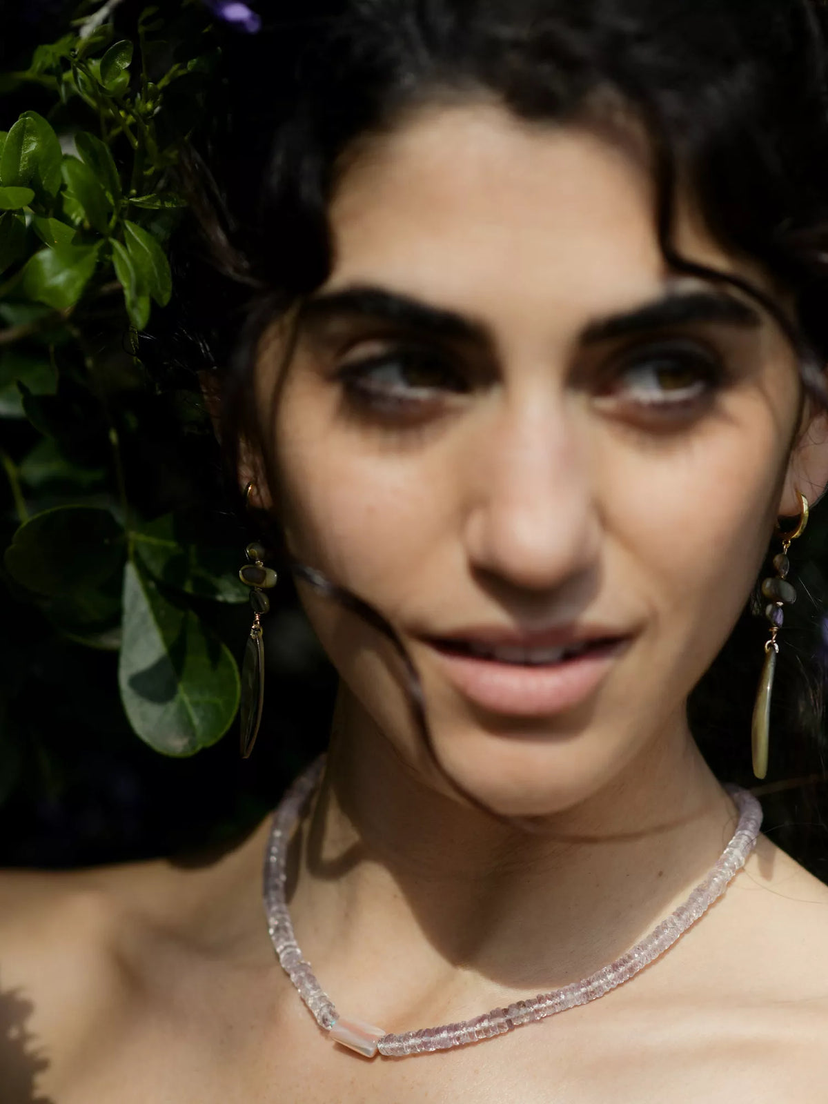 Close-up of a woman wearing a necklace with greenery in the background