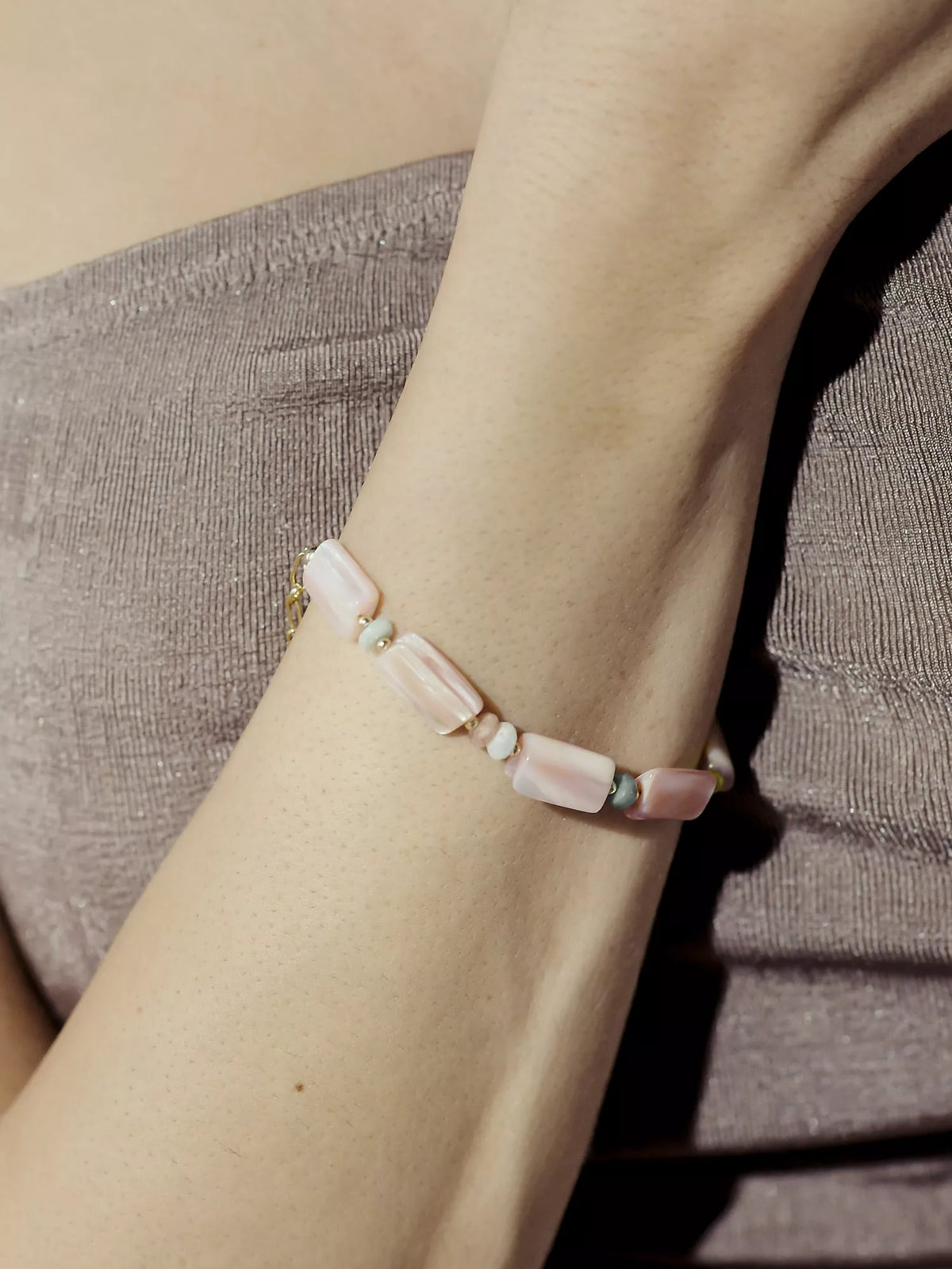 Close-up of a wrist wearing a pink beaded bracelet on a neutral background