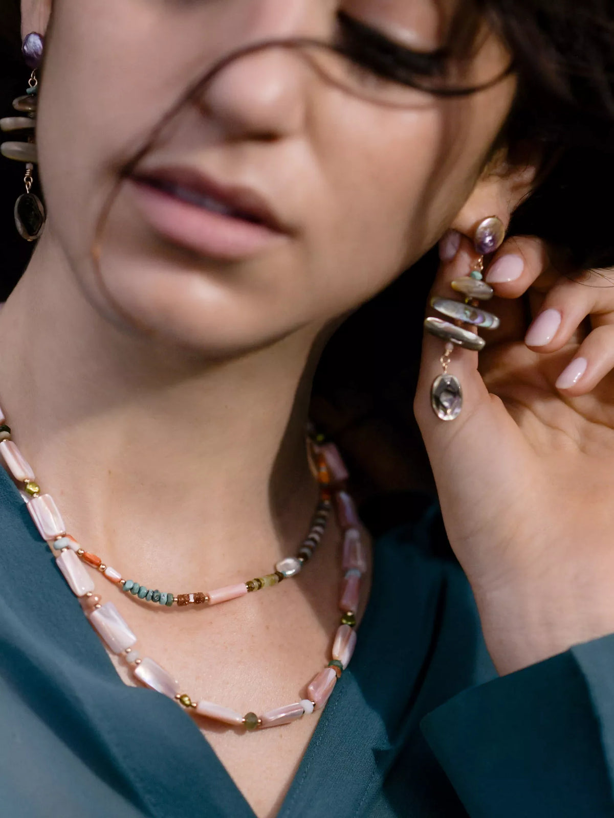 Close-up of a person wearing a beaded necklace and adjusting an earring.
