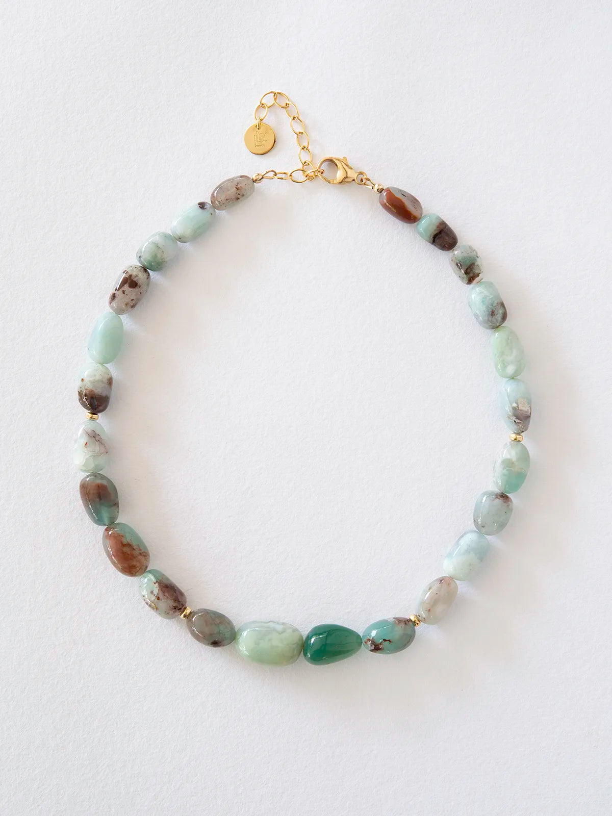 A beaded necklace featuring light green aquaprase, accented with gold spacer rings and a gold clasp on a white background.