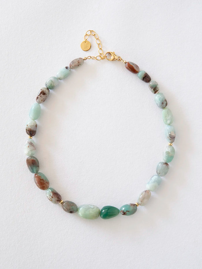 A beaded necklace featuring light green aquaprase, accented with gold spacer rings and a gold clasp on a white background.