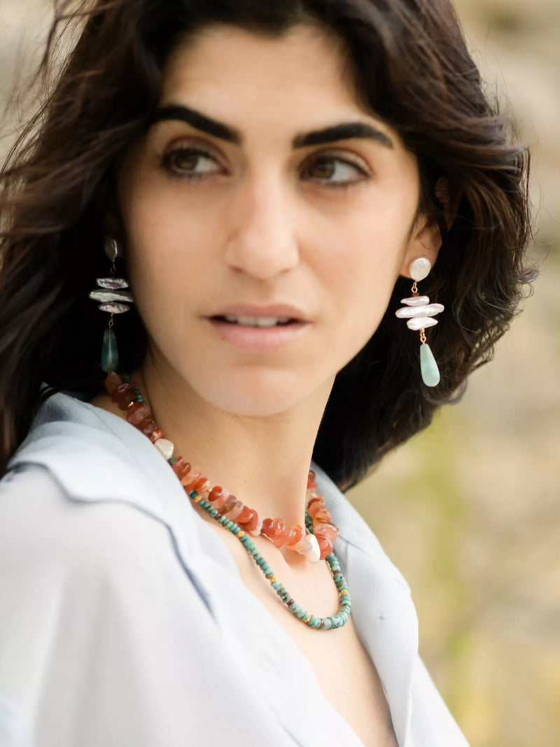 Woman wearing a necklace and earrings with a blurred natural background