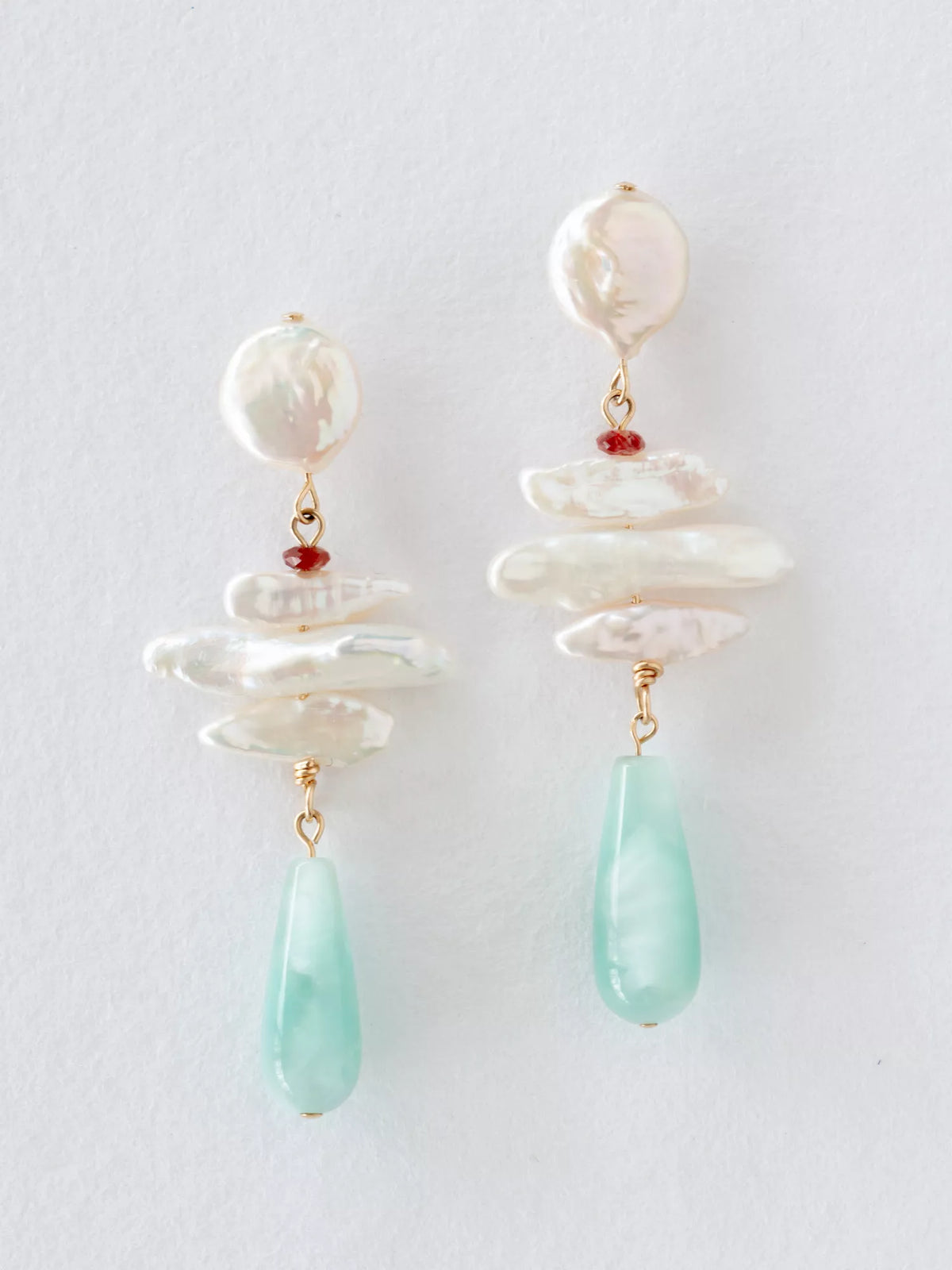 Pair of earrings with white pearls and green teardrop beads on a light gray background