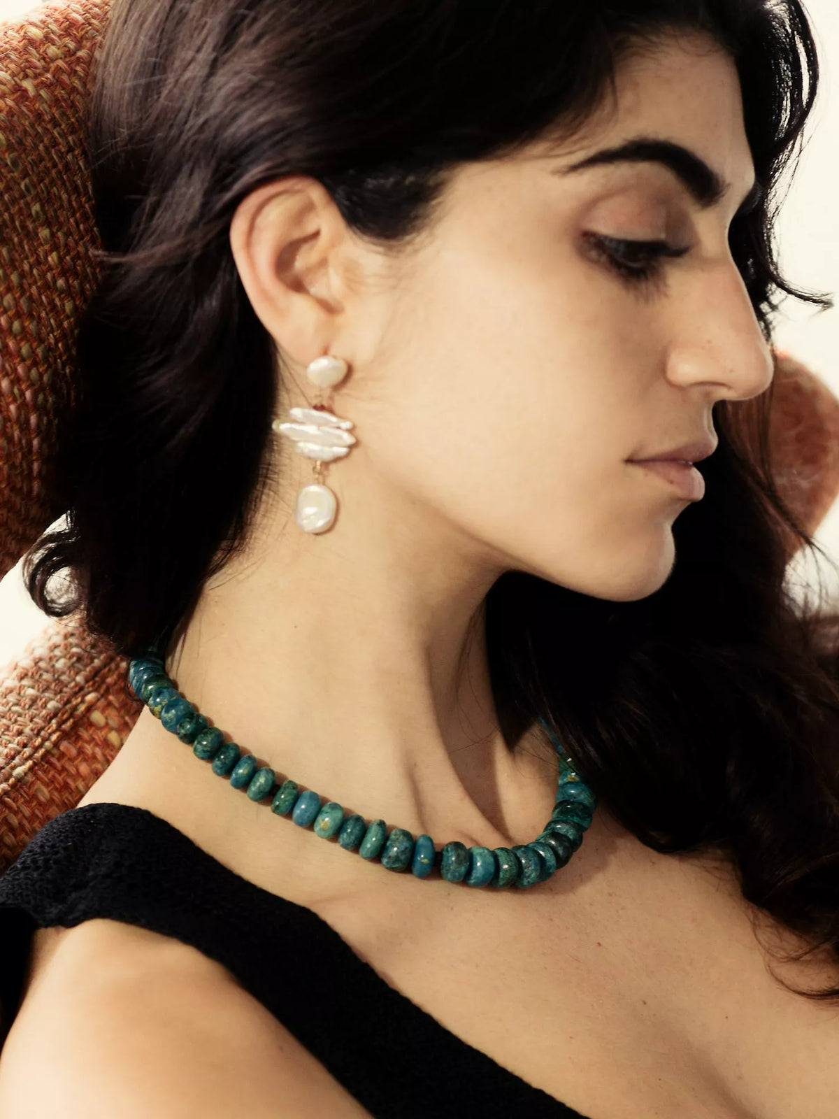 Woman wearing a teal beaded necklace and pearl earrings.