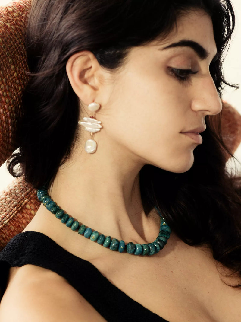 Woman wearing a teal beaded necklace and pearl earrings.