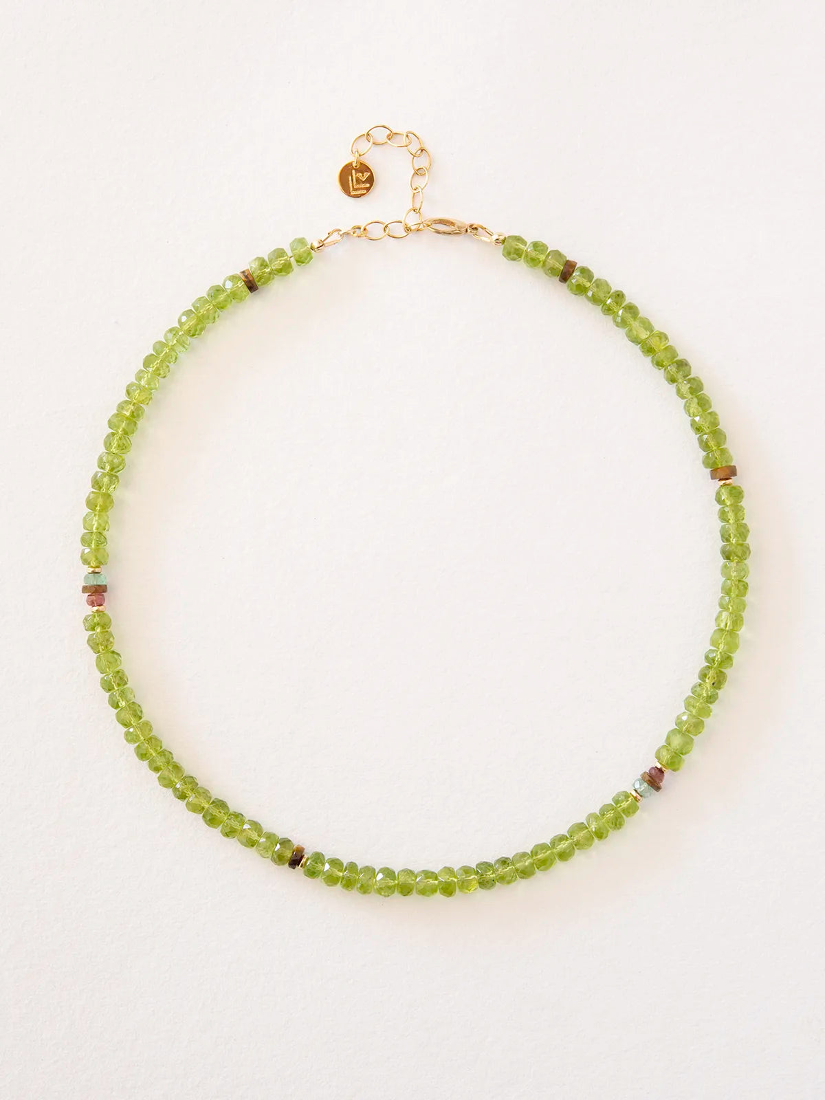 A beaded necklace made of small green faceted beads with a gold clasp and extender chain, photographed on a plain light background.