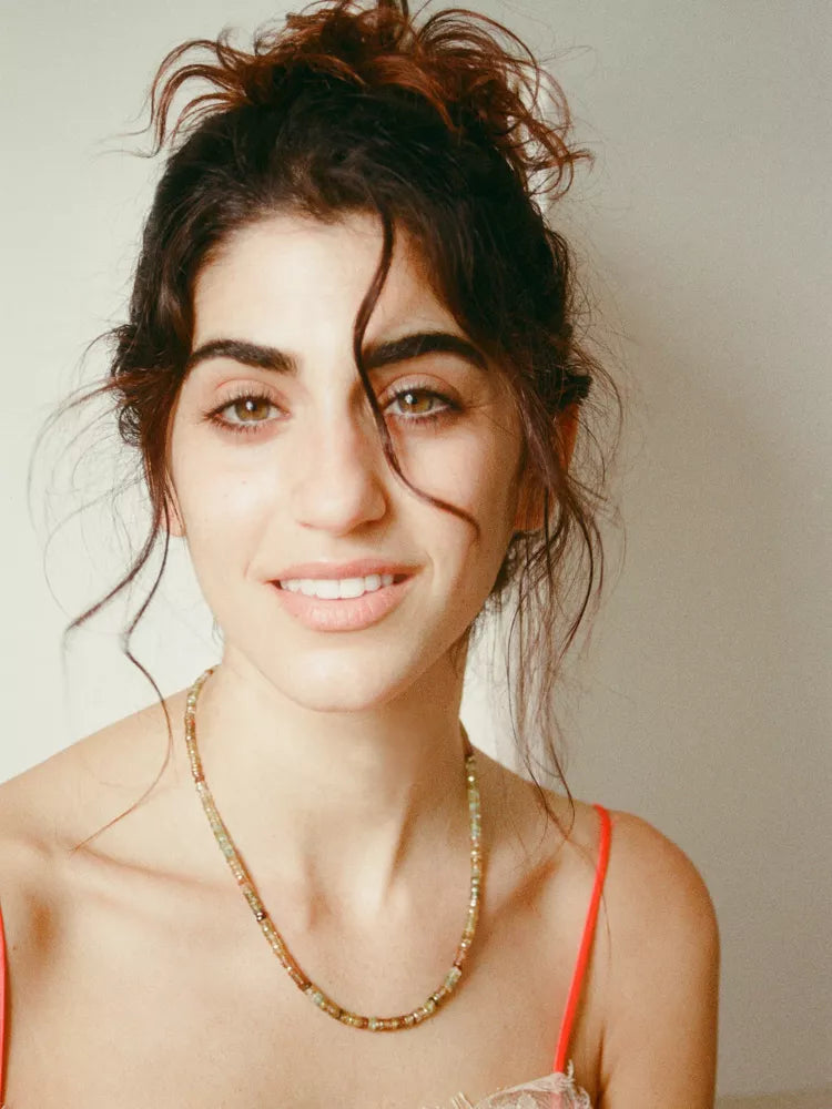 Woman with unstyled hair and a necklace against a neutral background
