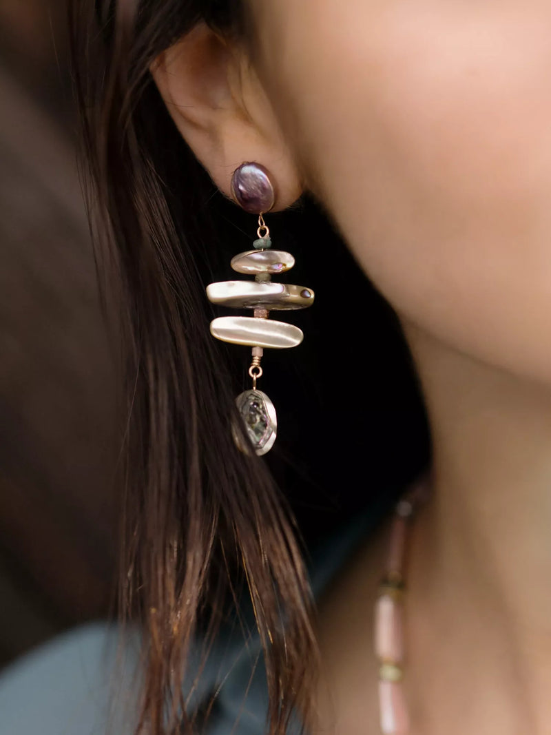 Close-up of a person wearing a unique earring with layered pearls and abalone.