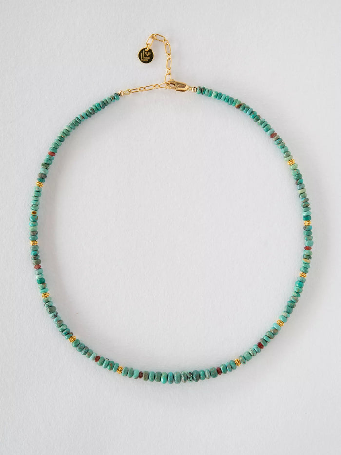 Necklace with turquoise beads and gold clasp on a light gray background